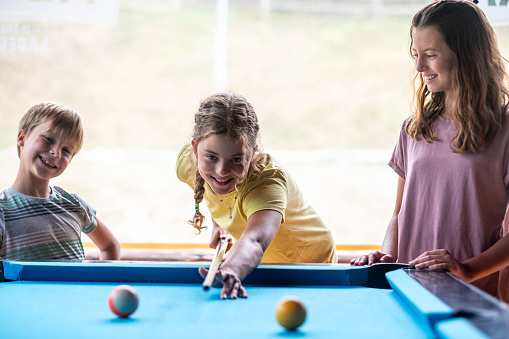 children play billiards and one girl hits the ball with a stick