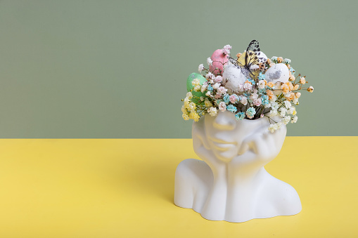 Plaster head statuette with Easter eggs and flowers. Easter creative concept.