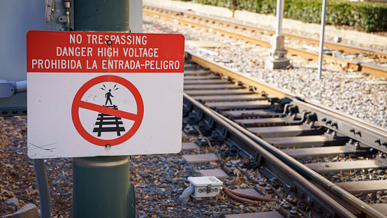 A sign warns of high voltage near the train tracks.