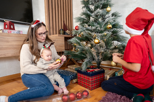 Mother decorating christmas tree at home with children