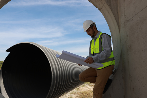 A structural engineer is standing at work at the end of a drainpipe.