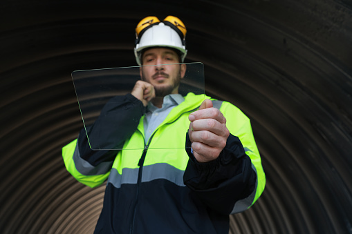 Mechanical engineer  with green reflective safety jacket and white hardhat working on clear screen, multi-purpose