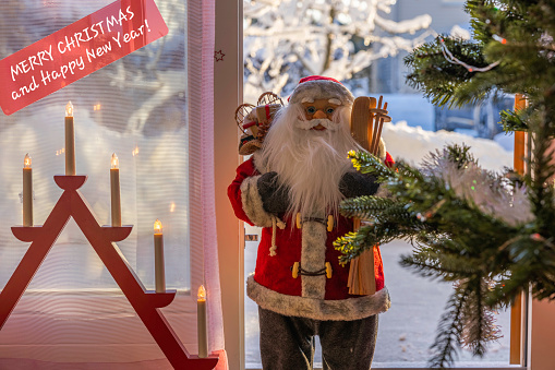 Beautiful Christmas view of Santa Claus with traditional electric candle, against backdrop of open door overlooking terrace and snow-covered garden. Sweden.