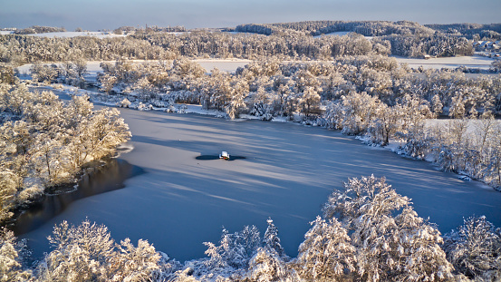 An aerial view of snow-covered trees surrounding a river in the middle of a forest.