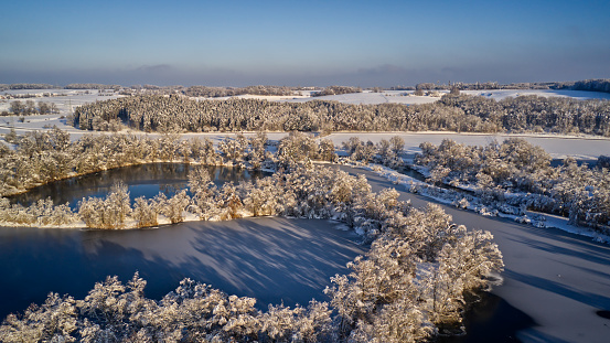 An aerial view of snow-covered trees surrounding a river in the middle of a forest.