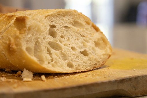 A freshly-baked loaf of bread is displayed on a wooden cutting board, with a sharp knife nearby, ready to be sliced