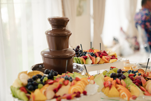 Three chocolate fountains decorated with an assortment of fresh fruit platters are displayed in a lavish display