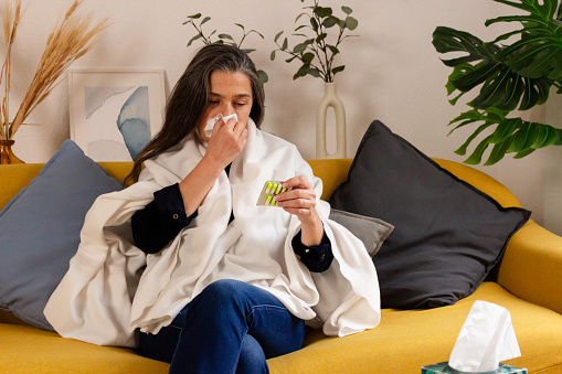 Sick woman with cold and flu sneezing in tissue at home