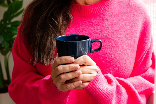Woman in pink sweater holding a blue cup of tea or coffee.