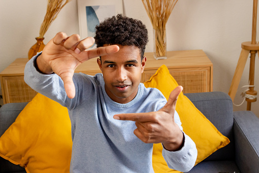 Young african american man making frame with fingers on sofa at home