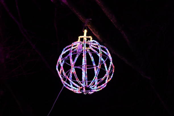 istock Christmas lights at night - large round multi coloured bauble hanging from a tree in a park 1883248348