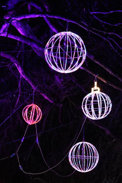 istock Christmas lights at night - large round multi coloured baubles hanging from a tree in a park 1883251881