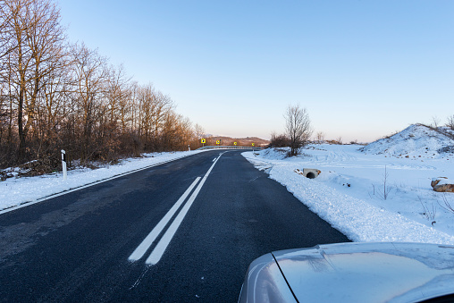 An empty two-lane highway. Winter scene. Empty asphalt road in rural landscape at sunset with blue clouds. Asphalt highway road with beautiful blue sky in pastoral rural environment.
