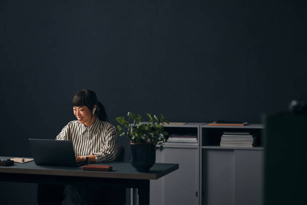 a happy beautiful asian teacher with earbuds working in the office on her computer - concentration teacher business copy space imagens e fotografias de stock