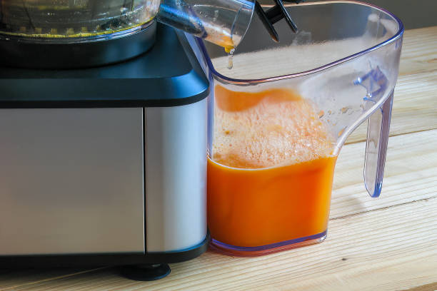 istock Tangerine juice flows out of juicer into juice container, close-up 1883368372