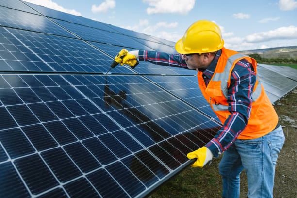 istock Efficient Repairs at the Solar Farm: Middle-Aged Energy Worker in Helmet and Vest Assembling Panels with Drill at a Natural Sun Energy Photovoltaic Farm Power Station Site 1883395162