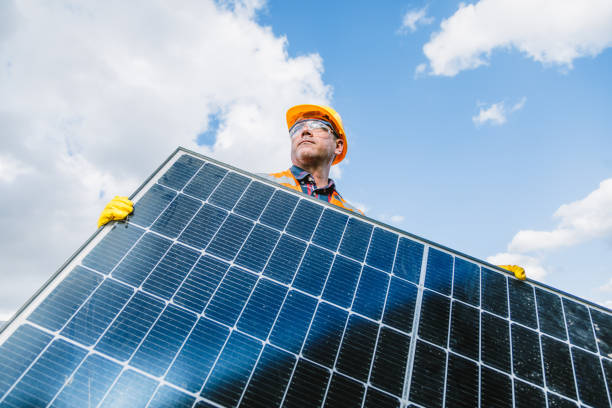 Embark on the future of solar energy with this compelling  featuring a male engineer wearing a reflective vest, confidently holding a solar panel in a solar photovoltaic farm power station. The image captures the dedication and precision required for deploying solar panels in a sustainable power generation environment. Ideal for conveying professionalism and commitment to clean energy initiatives, this photo is perfect for energy-related promotions, engineering publications, and social media content celebrating advancements in sustainable power. Male engineer, Reflective vest, Holding, Solar panel, Photovoltaic farm, Power station, Dedication, Precision, Clean energy,  Energy-related promotions, Engineering publications, Social media, Sustainable power