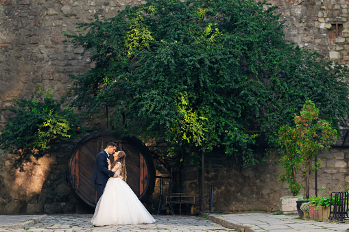 profile of newlyweds on the background of wall, barrels and tree.