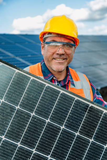 istock Solar Maintenance Expert: Portrait of Smiling Maintenance Worker Man Holding a Solar Panel Module in Photovoltaic Farm Power Energy Station 1883418491