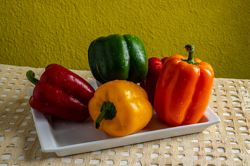 Bell peppers or peppers, of various colors, green, yellow and red, on a white plate, freshly cut, and moistened by rinsing them.
