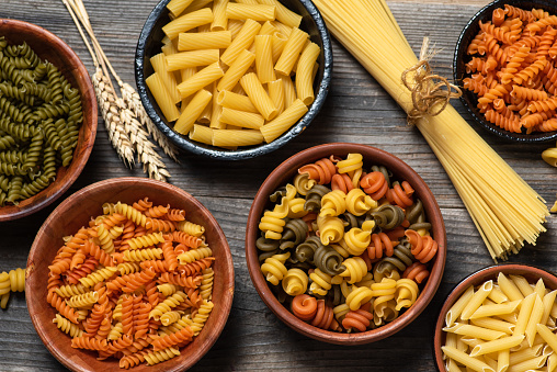 Variety of types, colors and shapes of Italian pasta in bowls, on a wooden table. Top view