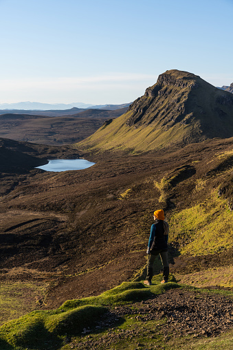 A woman hiking in the mountain range of the Quiraing on the Isle of Skye, Scotland, on a sunny day of springtime.