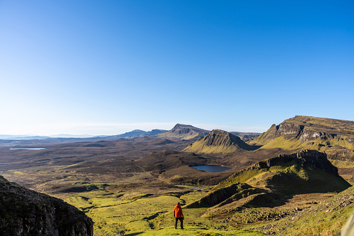 A man hiking in the mountain range of the Quiraing on the Isle of Skye, Scotland, on a sunny day of springtime.