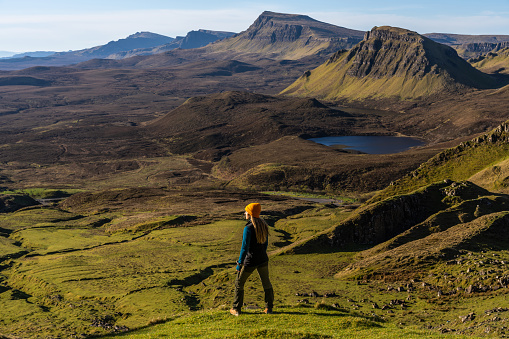 A woman hiking in the mountain range of the Quiraing on the Isle of Skye, Scotland, on a sunny day of springtime.
