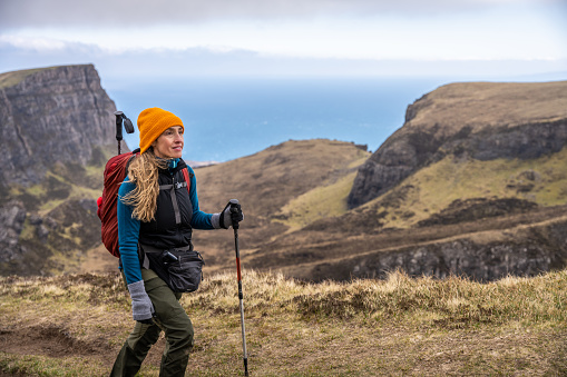 A woman hiking in the mountain range of the Quiraing on the Isle of Skye, Scotland, on a cloudy day of springtime.