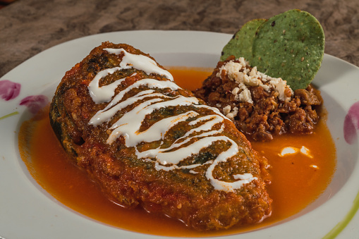 Detail of Chiles Rellenos, typical Mexican dish, poblano chiles stuffed with ground meat, Oaxaca cheese, covered with egg, accompanied by tomato caldillo and cream beans with tortilla chips.