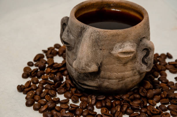 istock Coffee cup in the shape of a head, pre-Hispanic style, with brewed coffee inside it and coffee beans below it and adorning the scene 1883704978