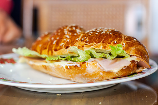 baker's hand showing a sandwich with open bread with cheese ham lettuce and mayonnaise on a plate on a table for breakfast