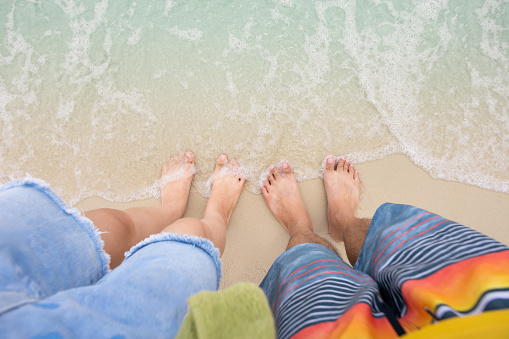 Man and woman feet are standing on the sandy beach with soft ocean wave.