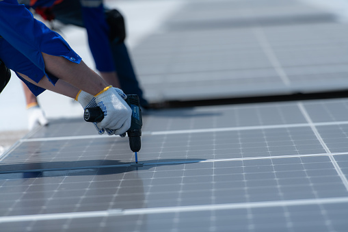 Both of technicians is installing solar panels on the roof of the warehouse to change solar energy into electrical energy for use in factories.