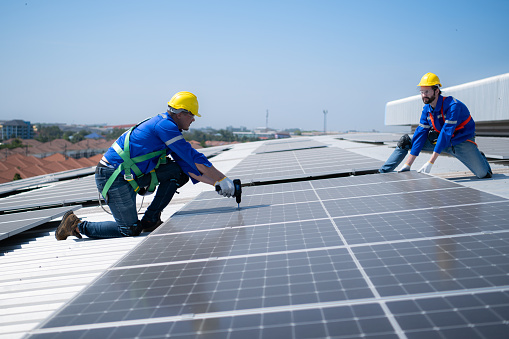 Both of technicians is installing solar panels on the roof of the warehouse to change solar energy into electrical energy for use in factories.