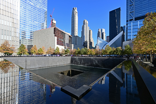New York City, New York - November 6, 2021 - Reflecting pool and surrounding buildings at National September 11 Memorial on cloudless autumn afternoon.
