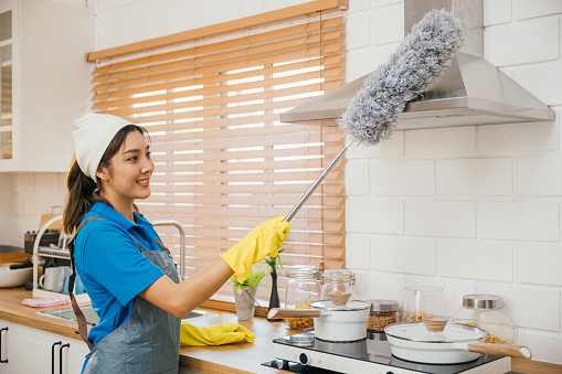 Asia woman in maid workwear gloves and apron cleans home dusts kitchen ventilation. Emphasizing housework modern hygiene equipment. Clean air whisk portrait. maid housekeeping concept.