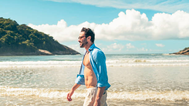 istock Man with an open shirt walking on the beach 1883840968