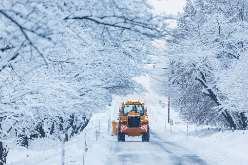 A rear view of a large snow plow machine clearing a country road lined with snow covered trees in Shizukuishi, North Japan.