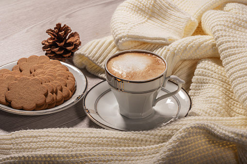 Cup of coffee, ginger cookies and warm white sweater on a white table. Cozy winter still life.