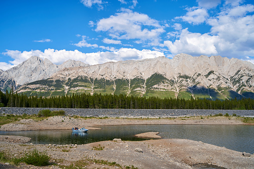 A fishing boat with fishermen fishing on a beautiful natural mountain lake on a sunny summer day with rocky mountains in the province of Alberta, Canada