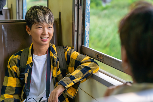 Group of Asian people friend enjoy and fun outdoor lifestyle travel in Thailand by railroad transportation on summer holiday vacation. Happy man and woman friends sitting on train and talking together