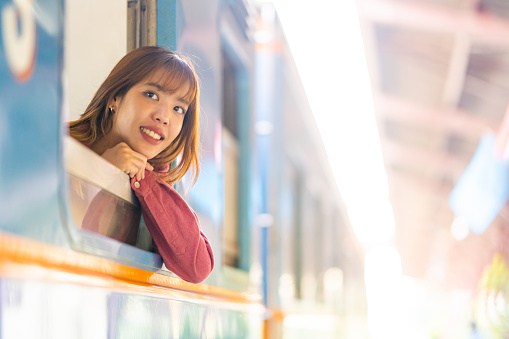 Portrait of Young Asian woman tourist sitting by the window on train. Attractive girl traveler enjoy and fun outdoor lifestyle travel on local railroad transportation on summer holiday vacation.