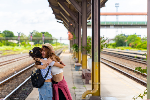 Happy Asian woman friends enjoy and fun urban outdoor lifestyle road trip travel countryside together on summer holiday vacation. Attractive girl meeting and hugging each other at railway station.