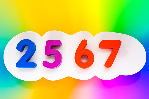 Image of colorful wooden block letters that convey the meaning of the upcoming 2567 Buddhist New Year on a beautiful multi-colored gradient background.