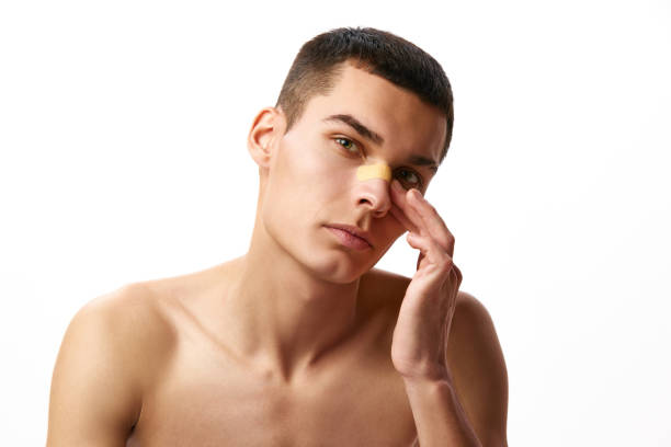 istock Rhinoplasty. Plastic surgery. Handsome young man with plaster on nose against white studio background 1884157244