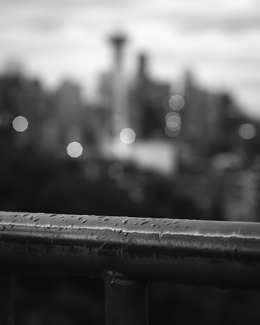 A vertical of a railing in raindrops against the cityscape of Seattle, Washington, USA in grayscale