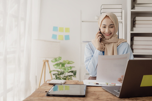 Beautiful Asian Muslim businesswoman uses smartphone to view social media application Answer chats with customers or discuss business transactions.