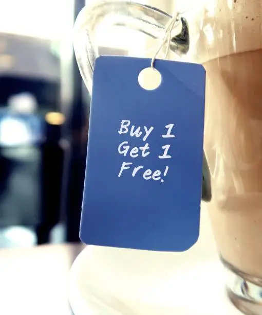 Photo of Blue tag hanging on coffee cup with text written BUY 1 GET 1 FREE, common form of sales promotion- deal involves offering a second product for the first price to attract customers