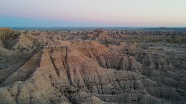 A 4K drone shot of the sharply eroded buttes in Badlands National Park, in Southwestern South Dakota, U.S.A. The camera slowly moves forward, rotates right, and pans up, over the rugged landscape.
